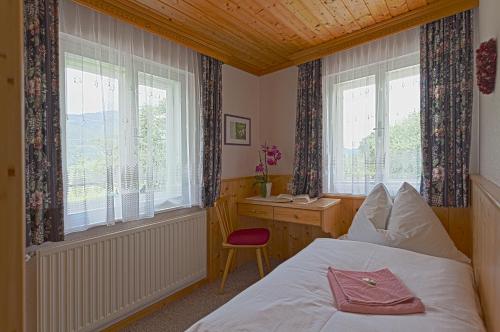 a bedroom with a bed and a desk and two windows at Moserhof in Haus im Ennstal