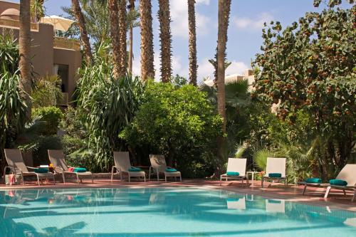 a swimming pool with chairs and palm trees at Les Jardins De La Médina in Marrakech