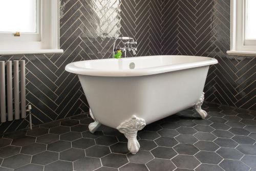 a white bath tub in a bathroom with black tiles at De Vere Beaumont Estate in Windsor