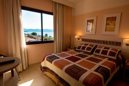 um quarto com uma cama e uma grande janela em Suítes e Studios no Hotel Jurerê Beach Village em Florianópolis