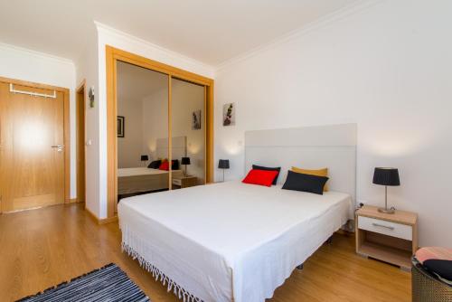 1 dormitorio con 1 cama blanca grande con almohadas rojas en Santa Luzia Residence Apartamento T2 com Piscina & Wi-Fi, en Santa Luzia