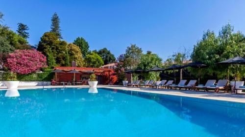 een groot zwembad met stoelen en parasols bij Hotel Quinta das Lagrimas - Small Luxury Hotels in Coimbra