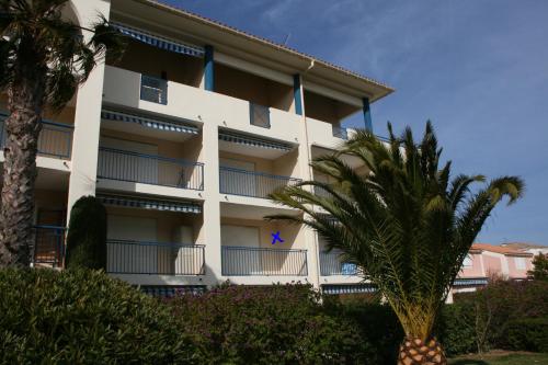 a white building with a palm tree in front of it at Résidence AZUR1 Appartement 251 in Le Lavandou