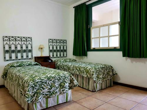 two beds in a room with green curtains and a window at Casa do Manequinho Hotel e Restaurante in Piraí