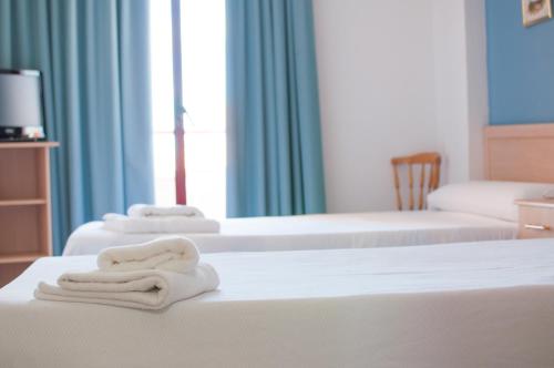 three white towels sitting on top of two beds at Hostal Concepción in La Mata