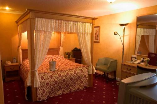a bedroom with a canopy bed and a chair at Wainstones Hotel in Stokesley