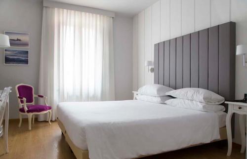 a bedroom with a large white bed and a purple chair at Hotel Serenella in Baveno