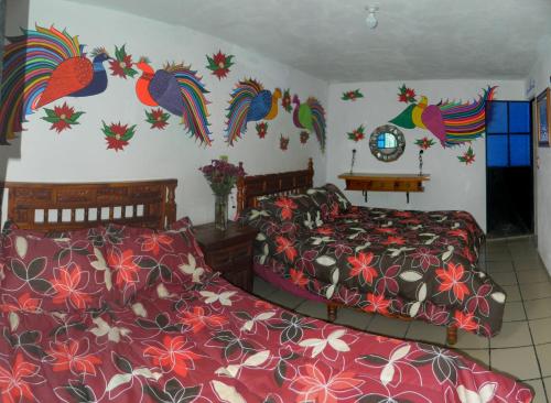 a bedroom with two beds and a wall with colorful birds at Posada Joan Sebastian in Taxco de Alarcón