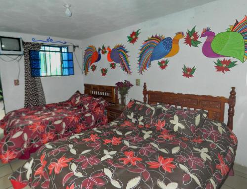 a bedroom with two beds and colorful birds on the wall at Posada Joan Sebastian in Taxco de Alarcón