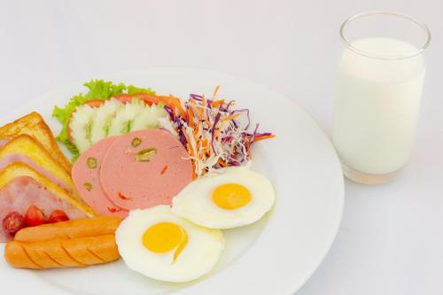 a plate of food with eggs and vegetables and a glass of milk at Grand Inter Hotel in Samut Sakhon