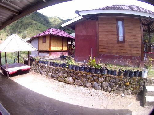a small house with a stone wall and an umbrella at Bale Sembahulun Cottages & Tend in Sembalun Lawang