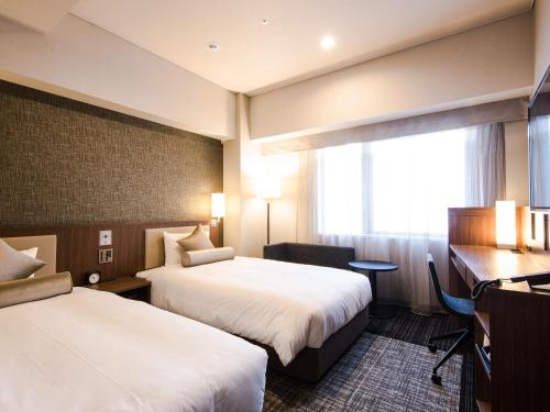 a hotel room with two beds and a desk and a window at HOTEL UNIZO Yokohamaeki-West in Yokohama