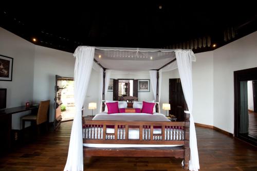 a bedroom with a canopy bed with pink pillows at Niraamaya Wellness Retreats, Surya Samudra, Kovalam in Kovalam
