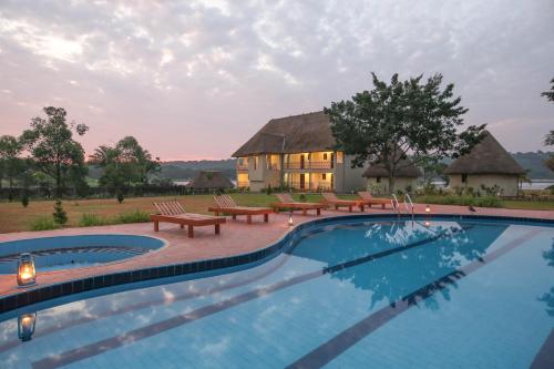 a swimming pool with benches and a house in the background at Victoria Forest Resort in Kalangala