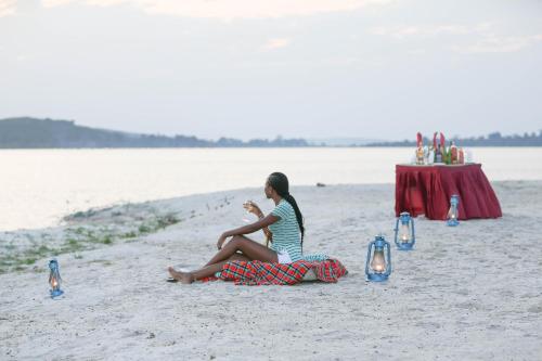 a woman sitting on the beach next to a table at Victoria Forest Resort in Kalangala