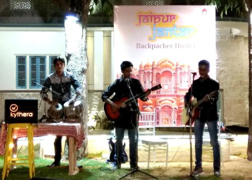 un grupo de tres hombres tocando instrumentos en un escenario en Jaipur Jantar Hostel, en Jaipur