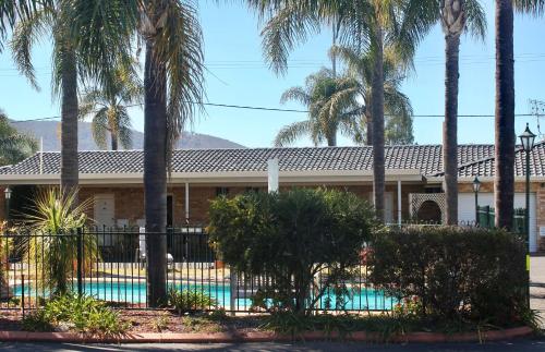 a house with a swimming pool and palm trees at Town and Country Motor Inn in Tamworth