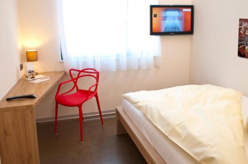 a red chair in a room with a desk and a bed at Hotel Credé in Kassel