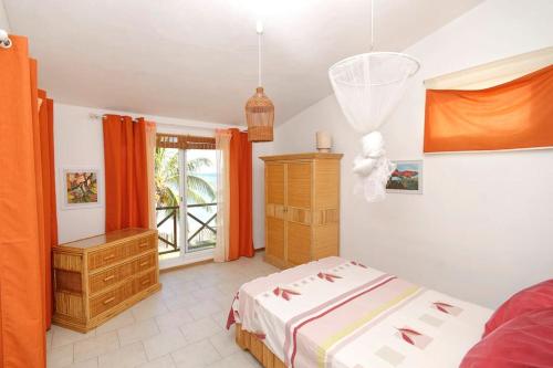 sypialnia z łóżkiem i oknem z pomarańczowymi zasłonami w obiekcie Villa Mauridul w mieście Baie du Tombeau