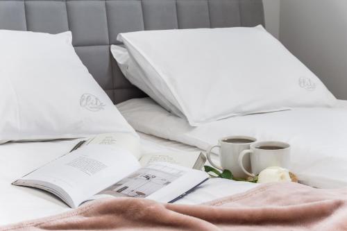 a bed with two white pillows and a book and cups at Elite Apartments Oliwa Business Center in Gdańsk