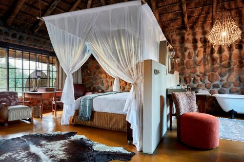 Geiger's Camp in Timbavati Game Reserve by NEWMARK في محمية صيد تيمبافاتي: غرفة نوم مع سرير مظلة وحوض استحمام