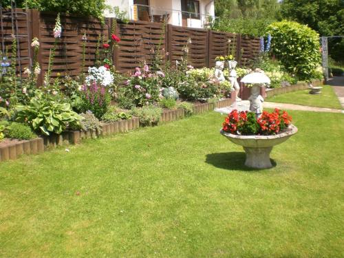 a garden with a bird bath with flowers and an umbrella at Gästehaus Wolf in Sierksdorf