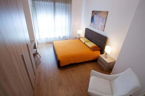 um quarto com uma cama laranja e uma cadeira branca em Nuovissimo e luminoso appartamento centro Pordenone em Pordenone