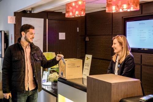a man and a woman standing at a counter with a box at Novotel Paris Sud Porte de Charenton in Charenton-le-Pont