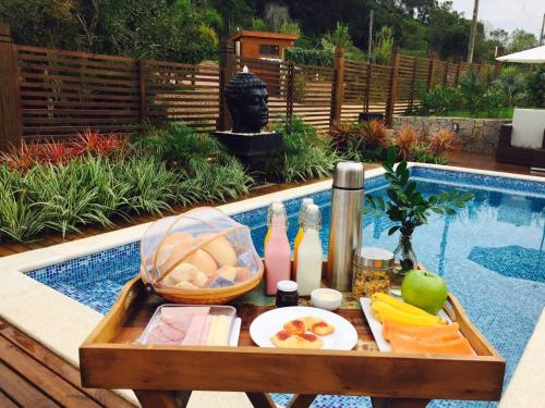 een dienblad met eten op een tafel naast een zwembad bij Pousada Vivenda do Rosa in Praia do Rosa