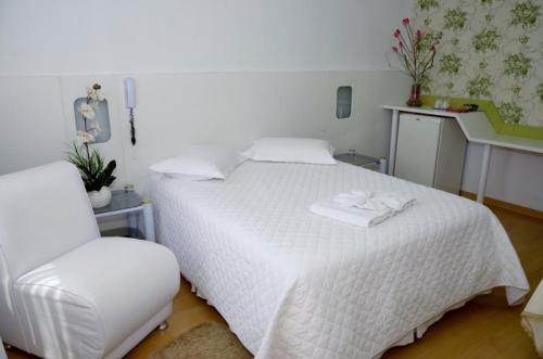 a bedroom with a white bed and a chair at Avenida Hotel in São Lourenço do Oeste