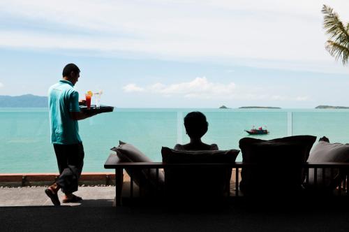 a man holding a tray of drinks in front of the ocean at Hansar Samui Resort & Spa - SHA Extra Plus in Bophut 