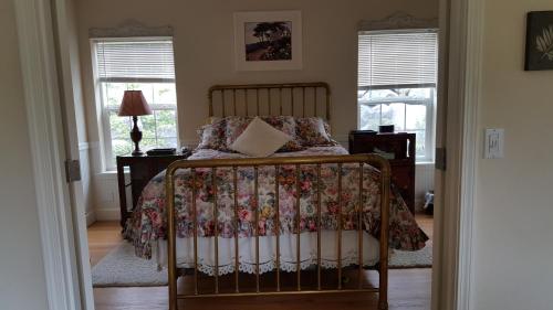 a bedroom with a bed with a floral bedspread and windows at Charming, Private Cottage in Myrtle Creek in Myrtle Creek
