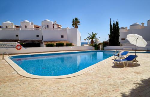 a swimming pool with chairs and an umbrella and a building at T2 Holiday Cottage near the beach C225 in Porches