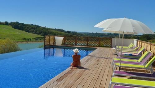 a person sitting next to a swimming pool with an umbrella at Résidence L'Oustal Del Carlat in Carla-Bayle