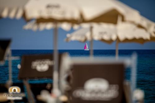 a sail boat in the ocean with umbrellas on a beach at Albergo Diffuso Mannois in Orosei