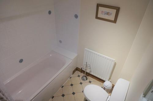 a white bathroom with a toilet and a bath tub at Waterside Cottages in Waterhouses
