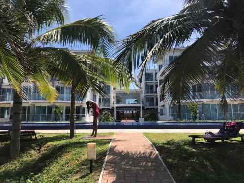a woman standing under a palm tree in front of a building at Araliya OceanFront Condos Nilaveli, Trincomalee in Nilaveli