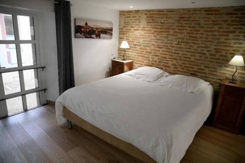 a bedroom with a white bed and a brick wall at Atout Carmes in Toulouse