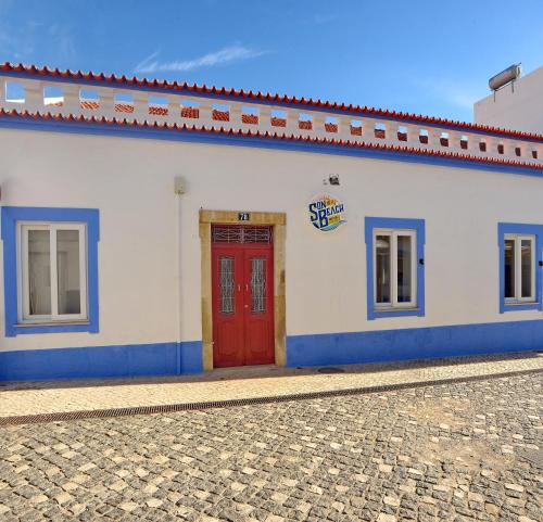 a white building with a red door on a street at Son of a Beach Hostel in Albufeira