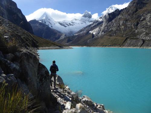 a man standing on the side of a blue lake at Caroline lodging in Huaraz