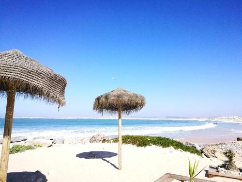 two straw umbrellas on a beach with the ocean at Peniche's Blue & White in Peniche