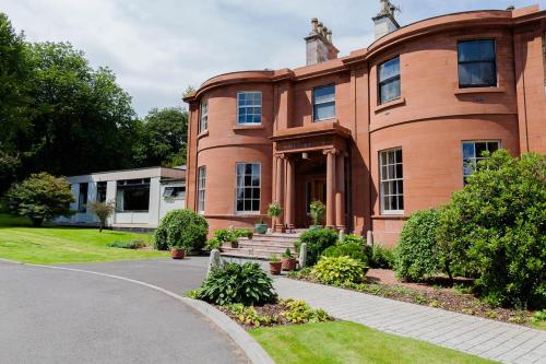 a large brick house with a driveway at Woodland House Hotel in Dumfries