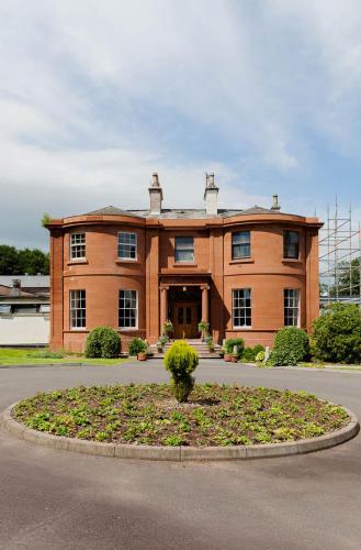a large brick building with a tree in front of it at Woodland House Hotel in Dumfries