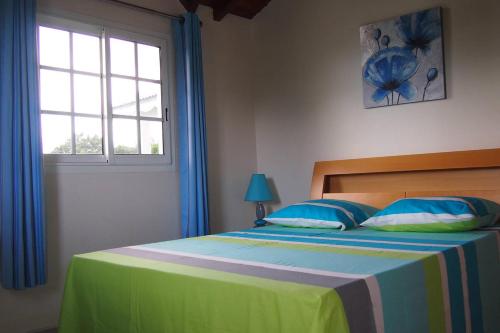 1 dormitorio con 1 cama con cortinas azules y ventana en Haut de villa, en Sainte-Rose