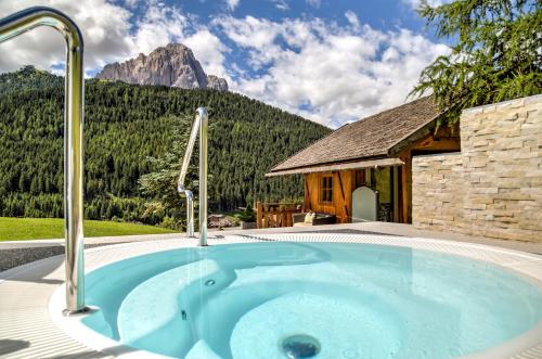 a hot tub in front of a house with a mountain at Hotel Fanes in Selva di Val Gardena