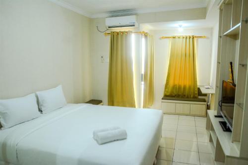 a bedroom with a white bed and a yellow curtain at Minimalist Studio Room at Grand Serpong Apartment By Travelio in Tangerang