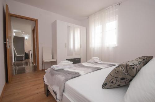 a white bedroom with a large bed and a window at Apartment Slad in Kaštela