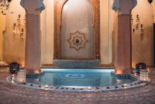 a swimming pool in a building with a fountain at Ambre Epices Medina Riad in Marrakech