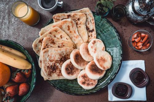a green plate with pancakes and fruit on a table at Ambre Epices Medina Riad in Marrakech
