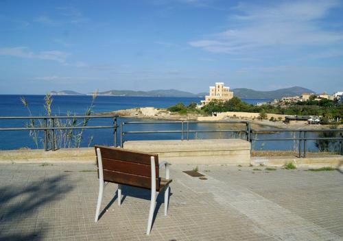 a wooden bench sitting on a sidewalk near the water at Alma di Alghero Apartments in Alghero